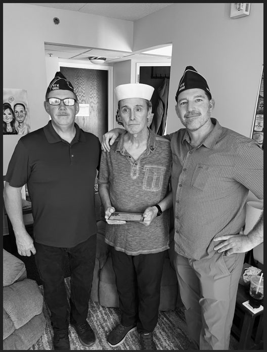 A Navy veteran in a sailor cap stands with two members of VFW Post 6896 after his Lily Hospice pinning ceremony